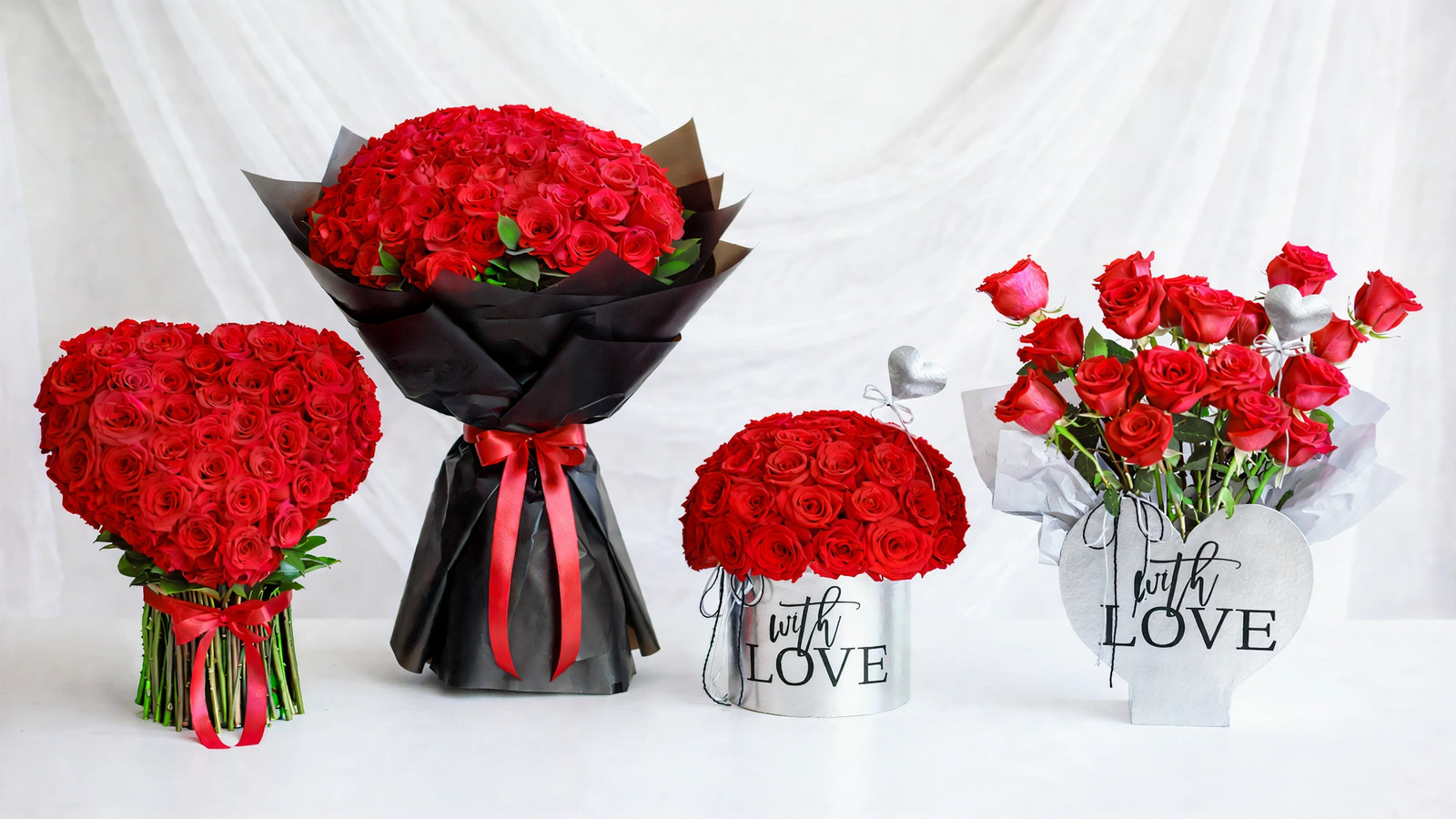 Four red rose arrangements side by side on white: a heart-shaped rose bouquet with red ribbon, a hundred-rose black-wrapped dome, a silver “with love” rose dome, and a “with love” heart box with red roses