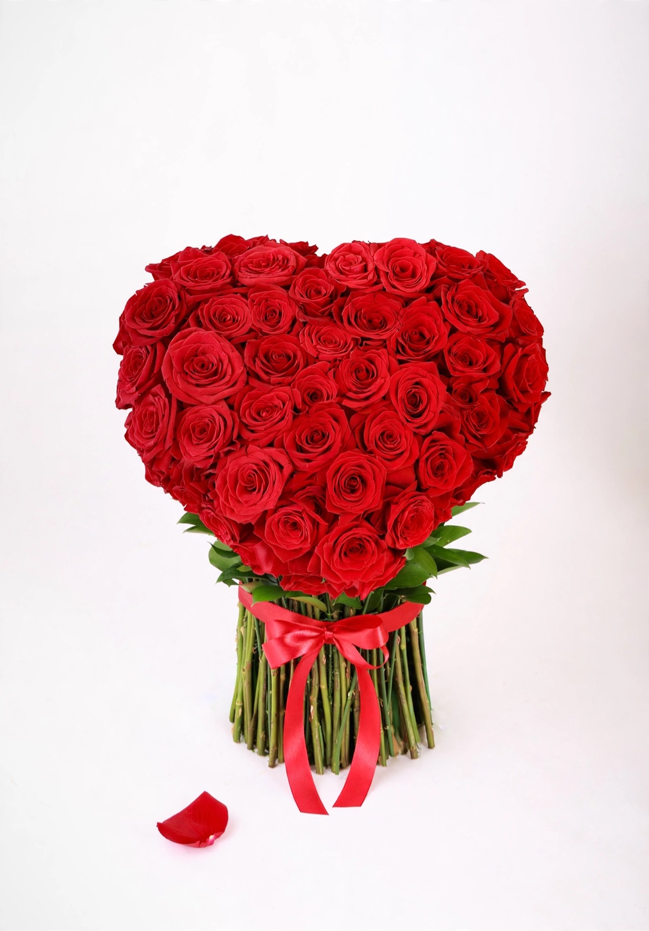 Heart-shaped arrangement of red roses on their stems, tied with a red satin bow